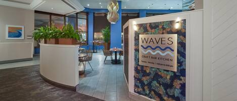 A reception area with a sign for 'WAVES Craft Bar Kitchen' and a seating area with tables and chairs.