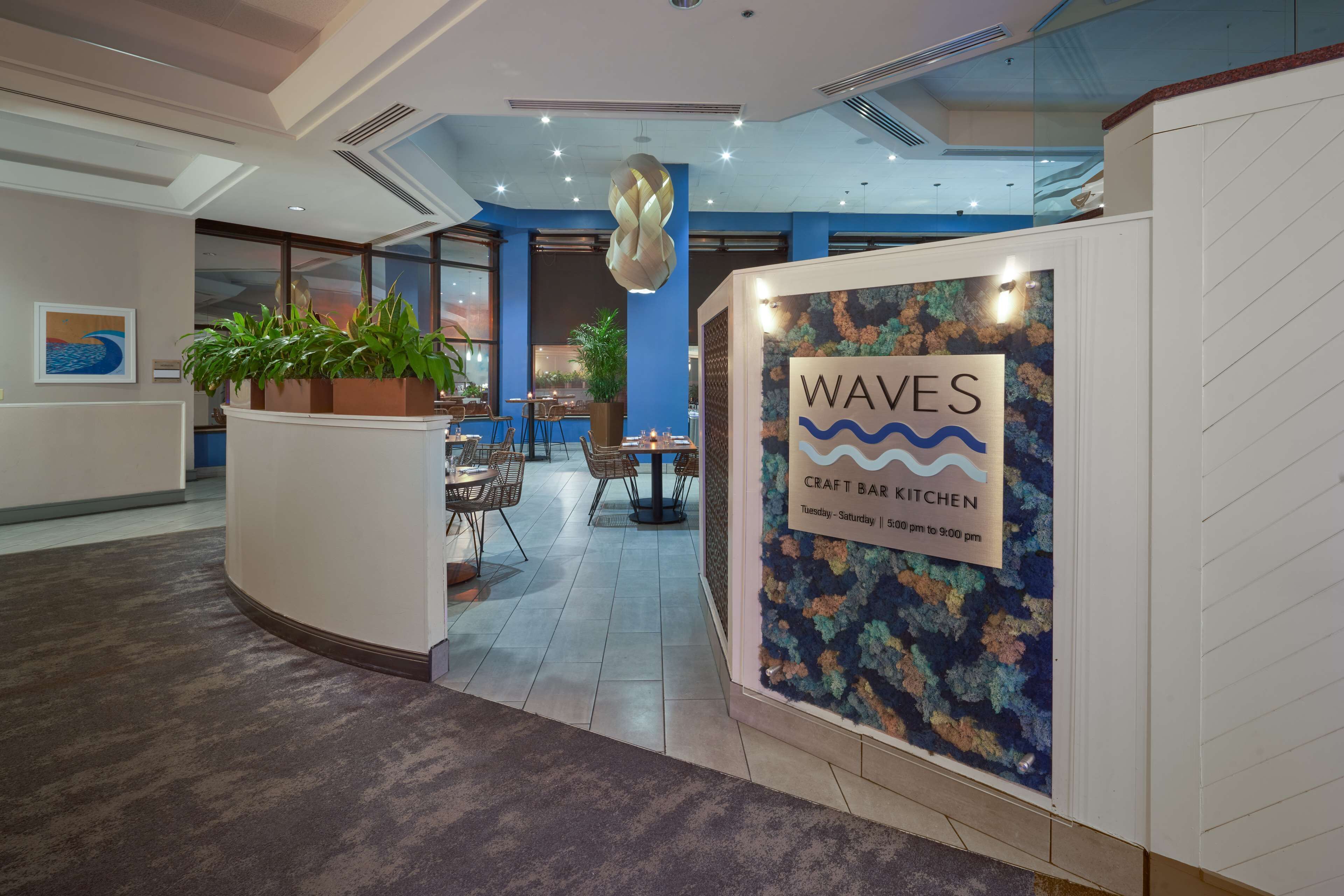 Un área de recepción con un letrero que indica 'WAVES Craft Bar Kitchen', abierta de martes a sábado de 17:00 a 21:00.