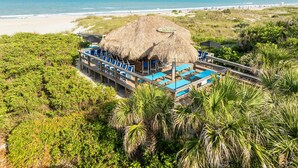 A beachside resort with a thatched-roof structure, multiple lounge areas with blue chairs, and a view of the ocean. - Hilton Cocoa Beach Oceanfront (Cocoa Beach)