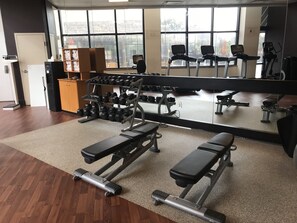 A gym with exercise equipment, a mirror, and windows. - Hilton Cocoa Beach Oceanfront (Cocoa Beach)