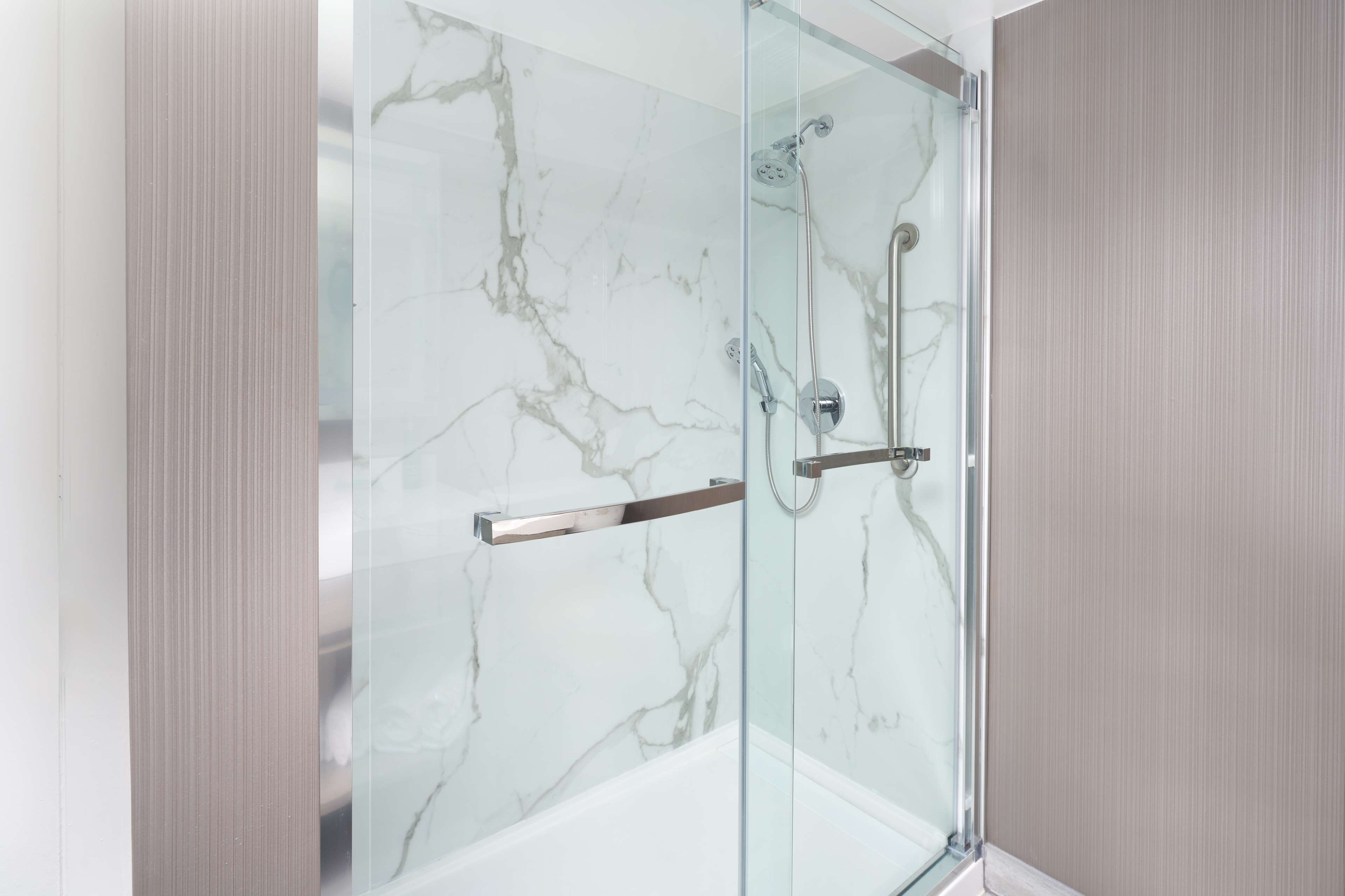 Eine gläserne Dusche mit Marmorwand und einem Metallgriff.