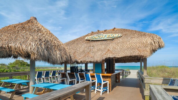 A beach bar with thatched umbrellas and wooden deck seating. - Hilton Cocoa Beach Oceanfront (Cocoa Beach)