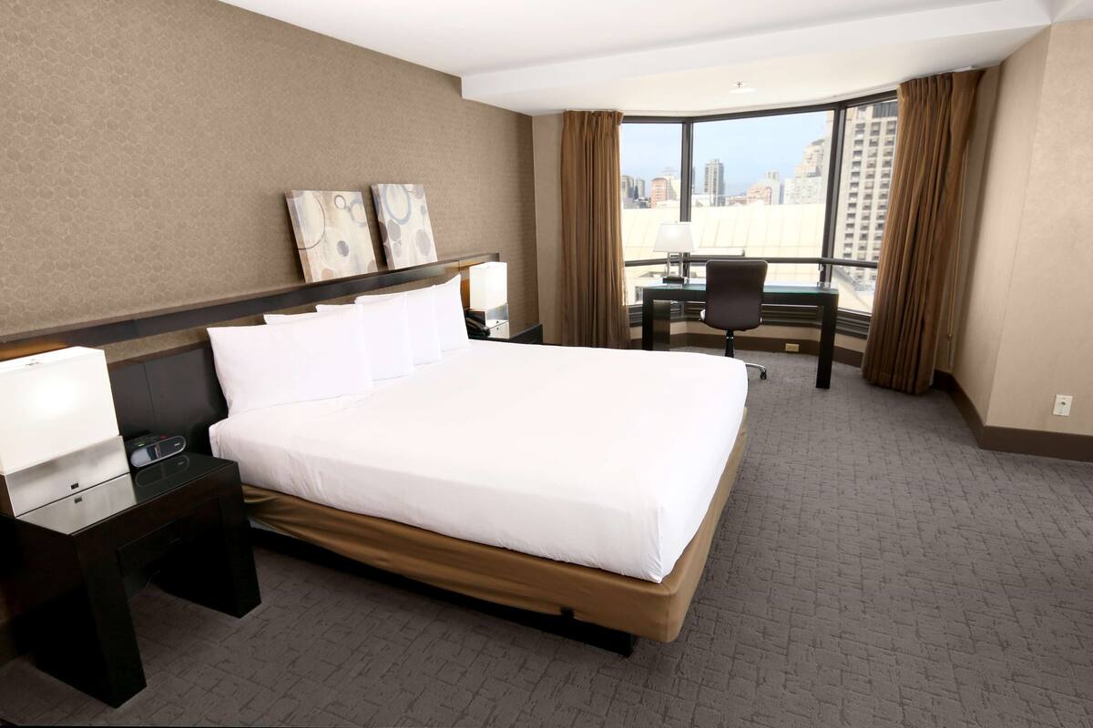 A hotel room with a large bed, a desk, and a view of the city.
