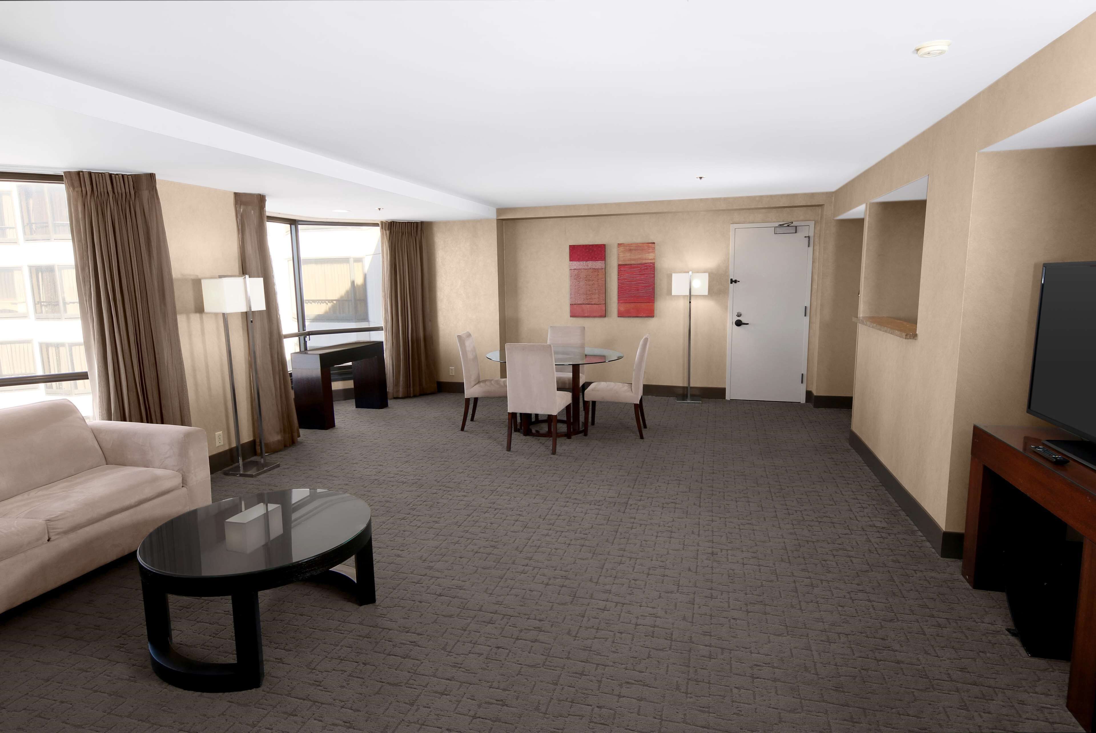 A hotel room with a sofa, a round table with chairs, a TV, and a door.