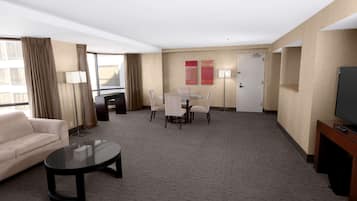 A hotel room with a sofa, a round table with chairs, a TV, and a door.