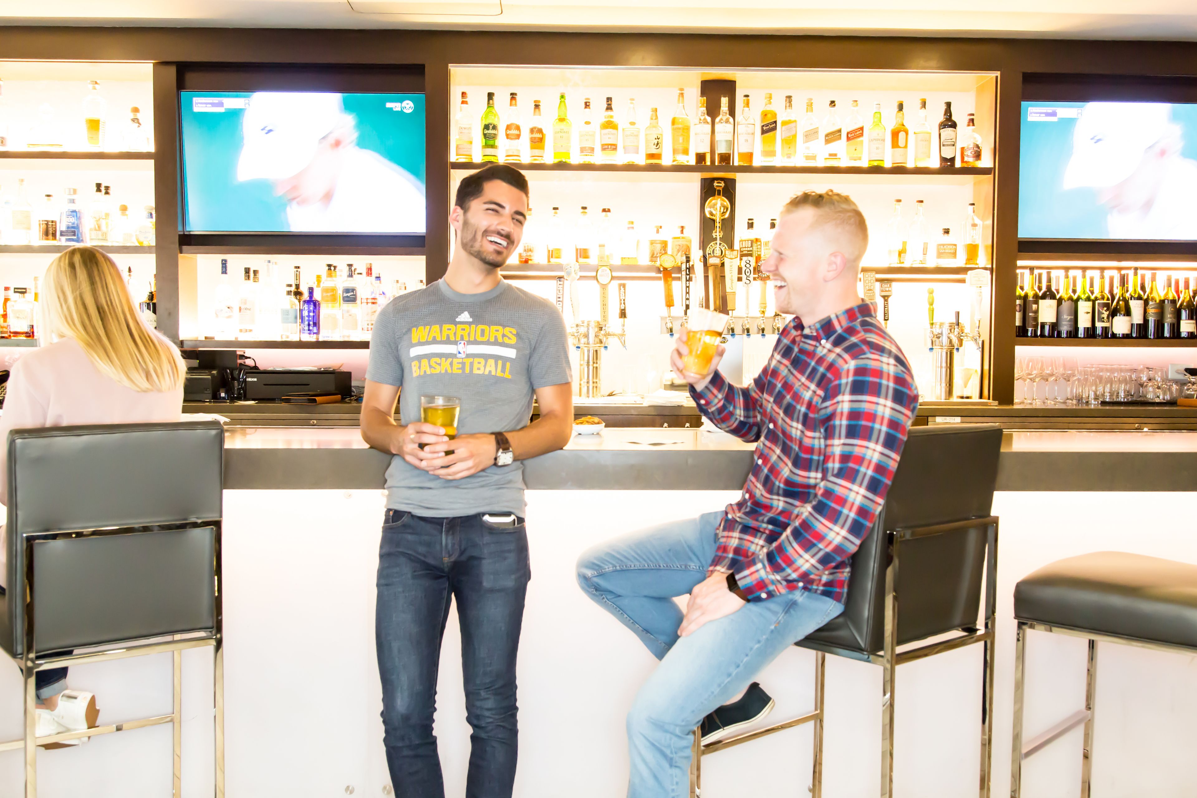 A bar area with multiple TVs, a variety of bottles, and bar stools.