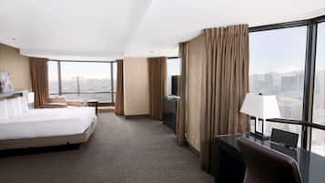 A hotel room with a large bed, a desk with a lamp, a TV, and a view of the city.