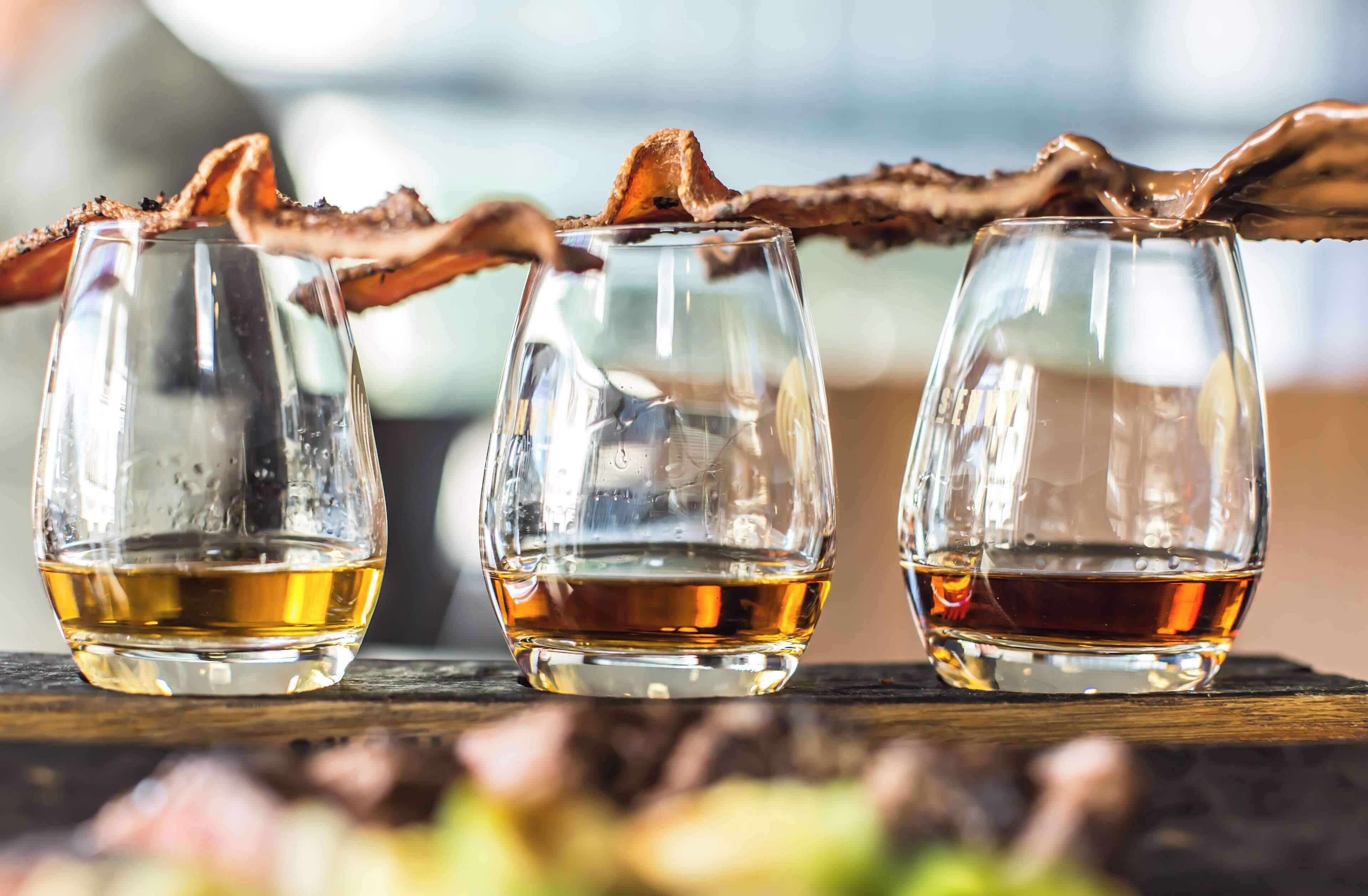 Three glasses of whiskey with a branch garnish on a wooden surface.