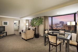 A hotel room with a city view, a sofa, a dining table with chairs, a TV, and a potted plant. - Parc 55 San Francisco - A Hilton Hotel (San Francisco)