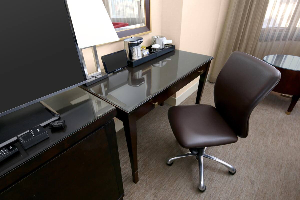 A hotel room with a desk, chair, and a window with curtains.