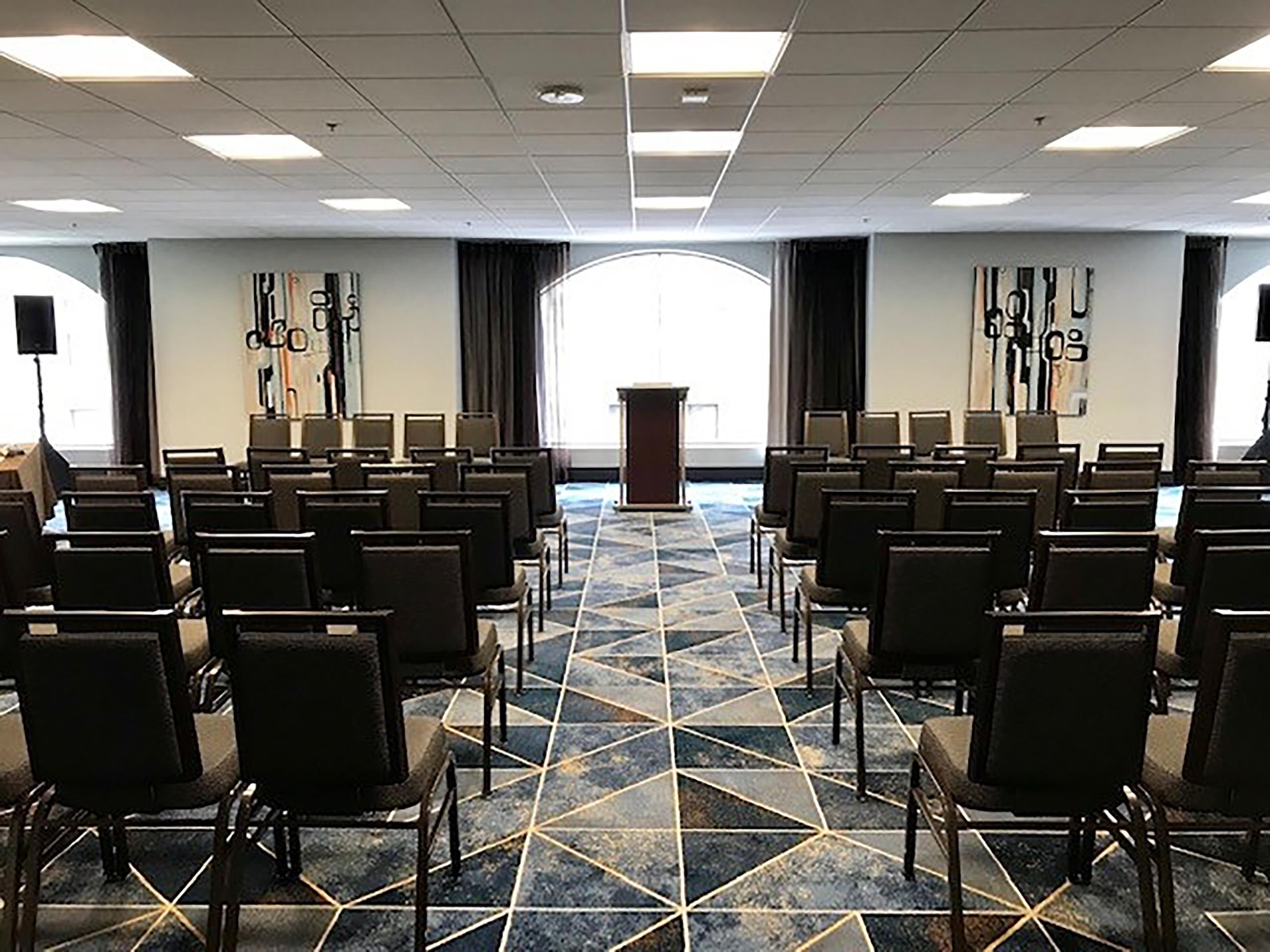 Une salle de conférence avec des rangées de chaises, un pupitre et une grande fenêtre avec des rideaux.