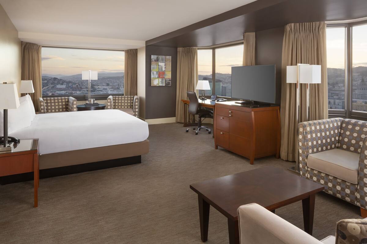 A hotel room with a large bed, a desk, a sofa, and a TV.
