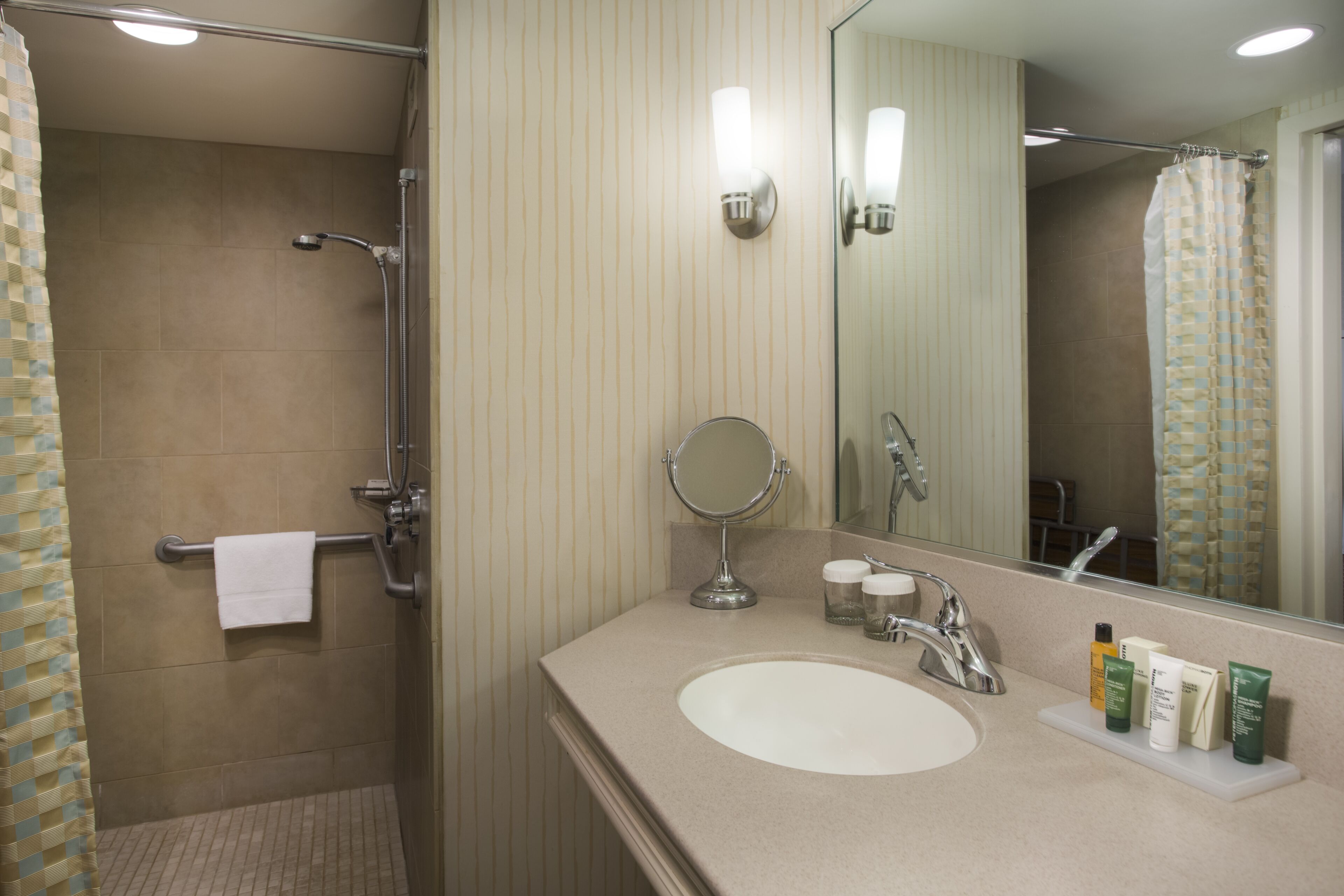 A bathroom with a shower, a sink with toiletries, and a mirror.
