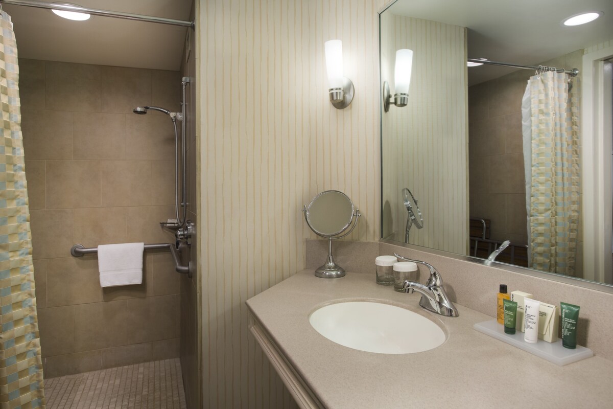 A bathroom with a shower, a sink with toiletries, and a mirror.
