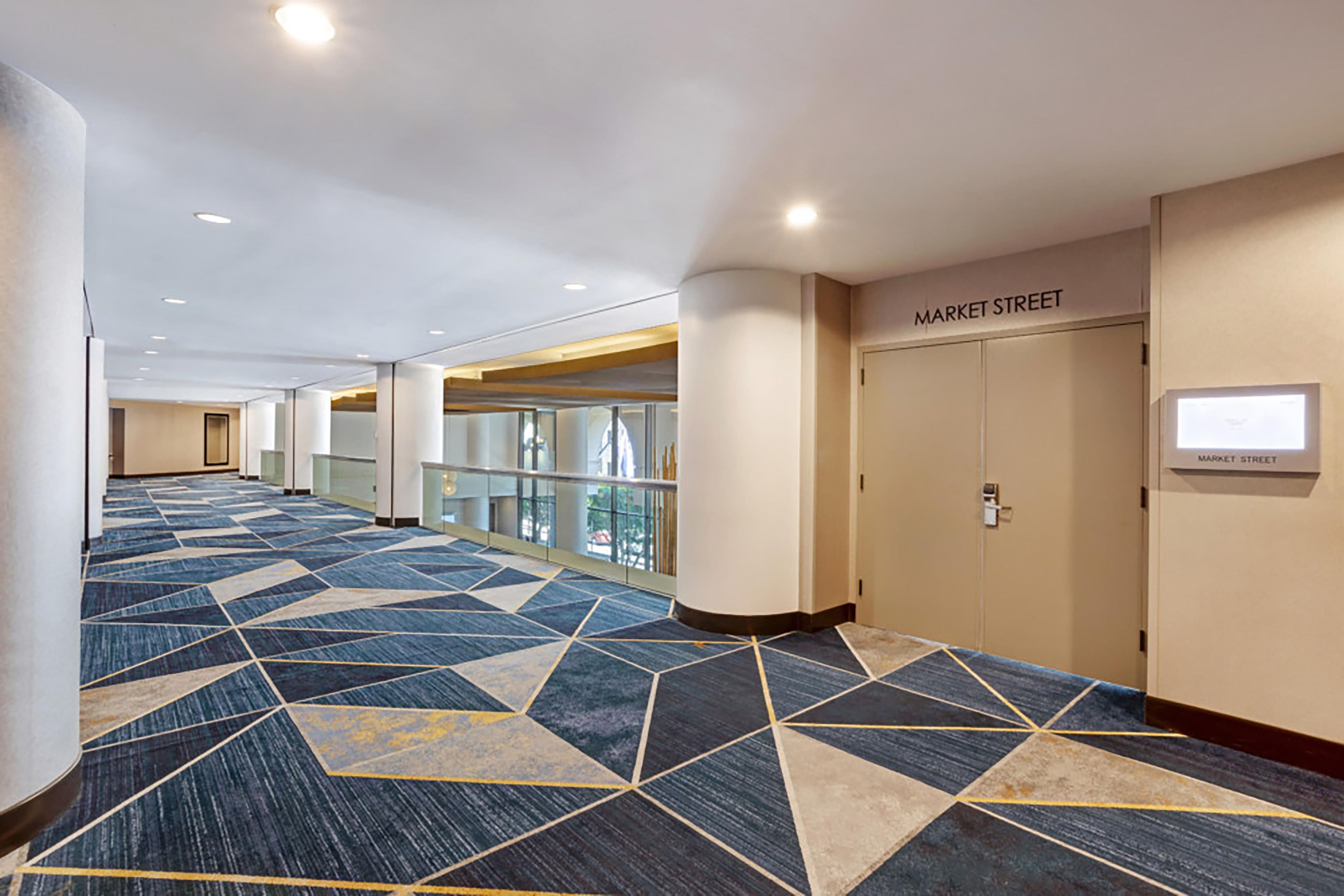 Ein Hotelgang mit Teppich im geometrischen Muster, einer Glasreling und Türen mit der Aufschrift 'MARKET STREET'.