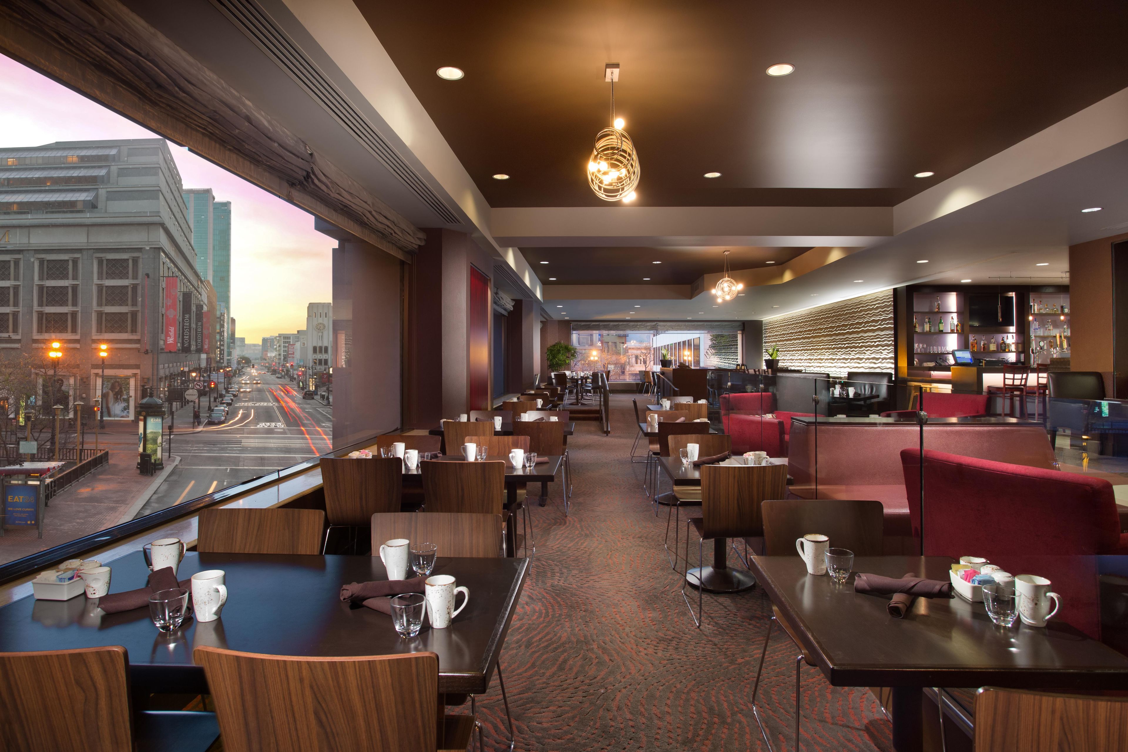 En moderne restaurant med flere siddeområder, herunder borde og båse, samt en bar med udsigt over bybilledet.