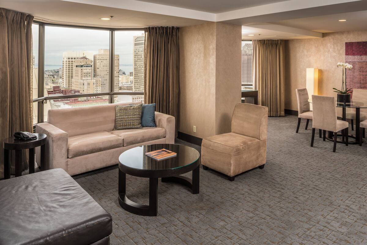 A hotel room with a sofa, armchair, dining table, and chairs.