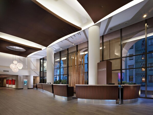 A modern hotel lobby with a reception desk, large windows, and a wooden reception desk.