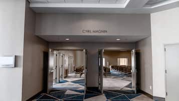 Et hotelbrugsgang med et geometrisk mønstret tæppe, døre der fører til et siddeområde, og et skilt med teksten 'CYRIL MAGNIN'.