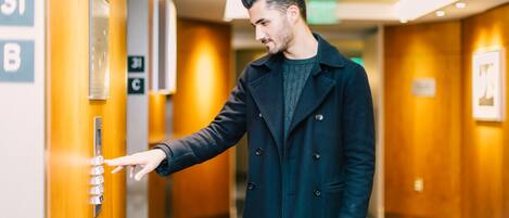 A man in a black coat interacting with an elevator control panel in a hotel hallway.