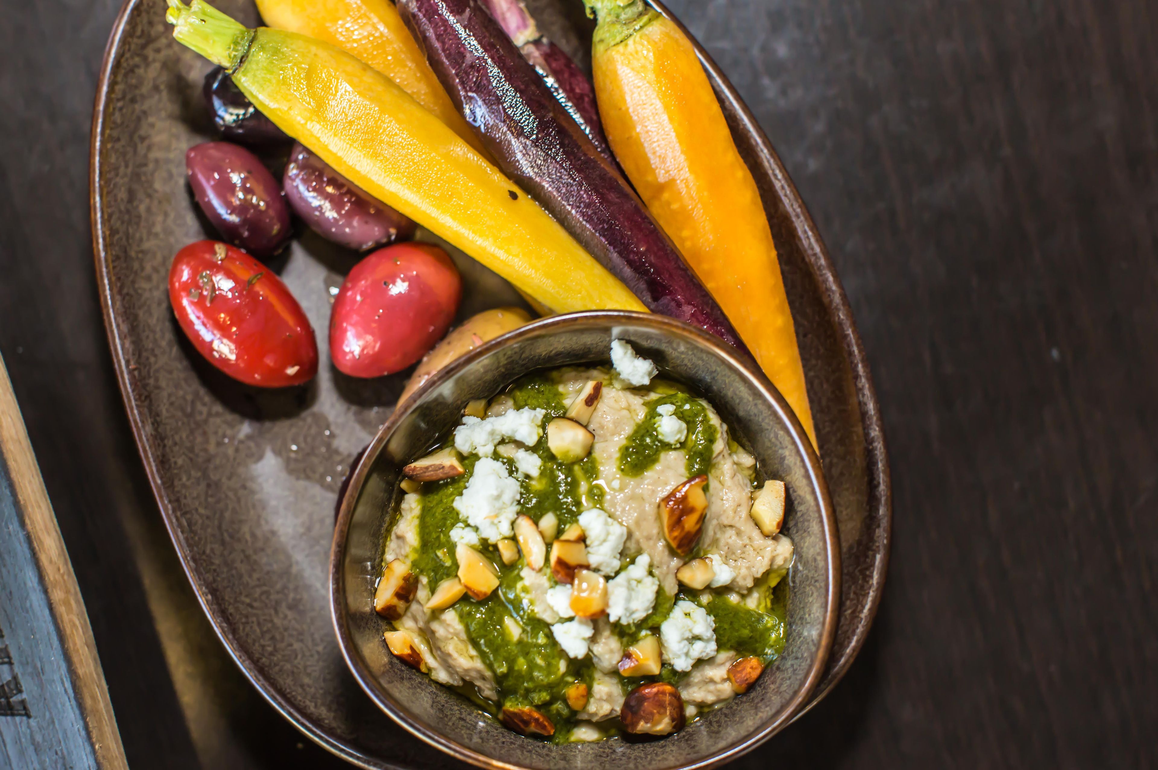 Un bol de trempette accompagné de noix et d’une variété de légumes, le tout présenté sur une assiette.
