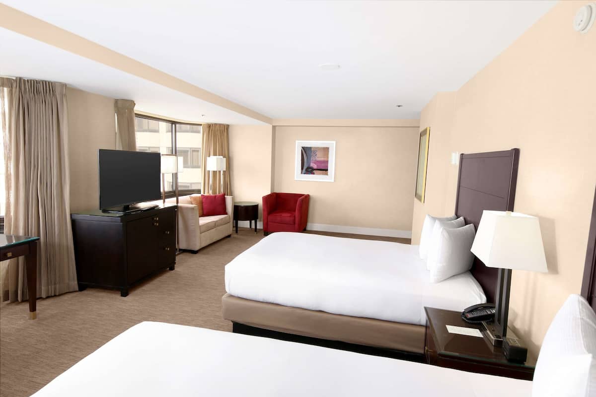 A hotel room with a bed, a TV, a desk with a lamp, a chair, and a small table.