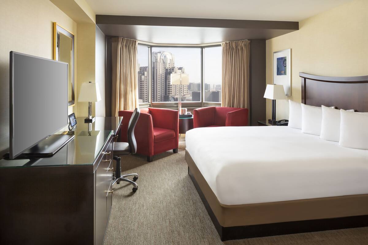 A hotel room with a large bed, a desk, a chair, and a TV.