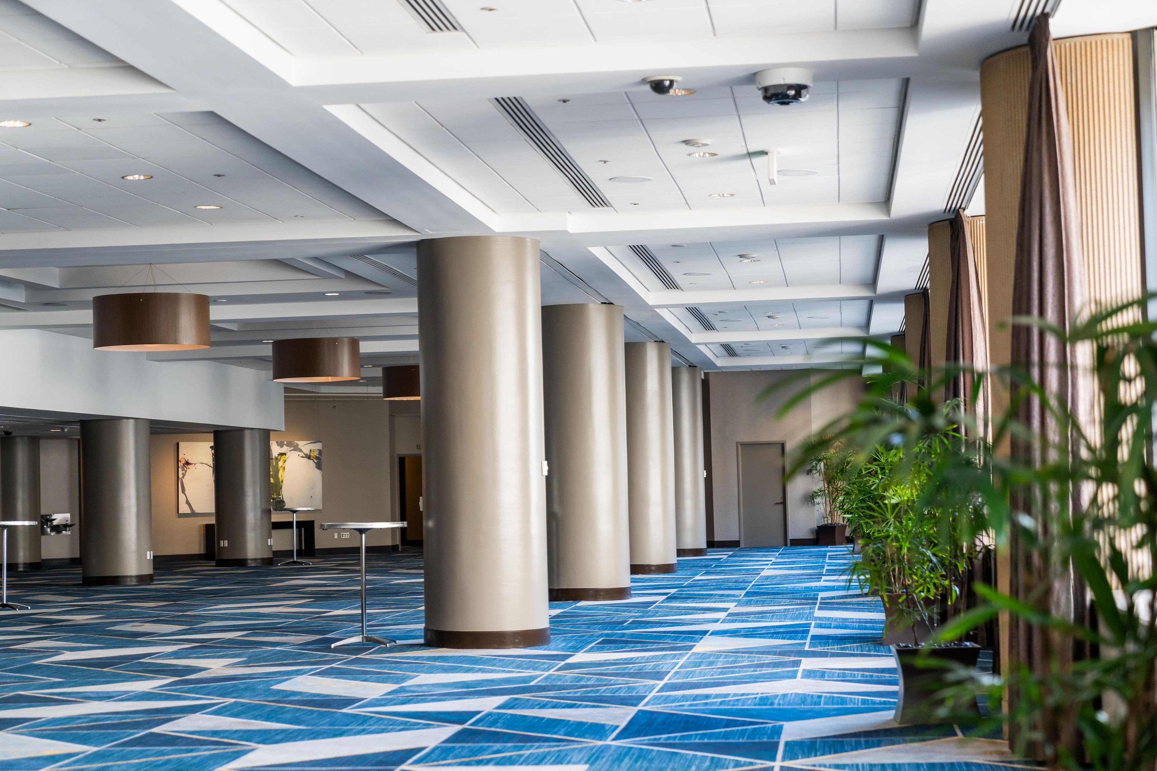 A spacious hotel lobby with high ceilings, large pillars, and a patterned blue carpet.
