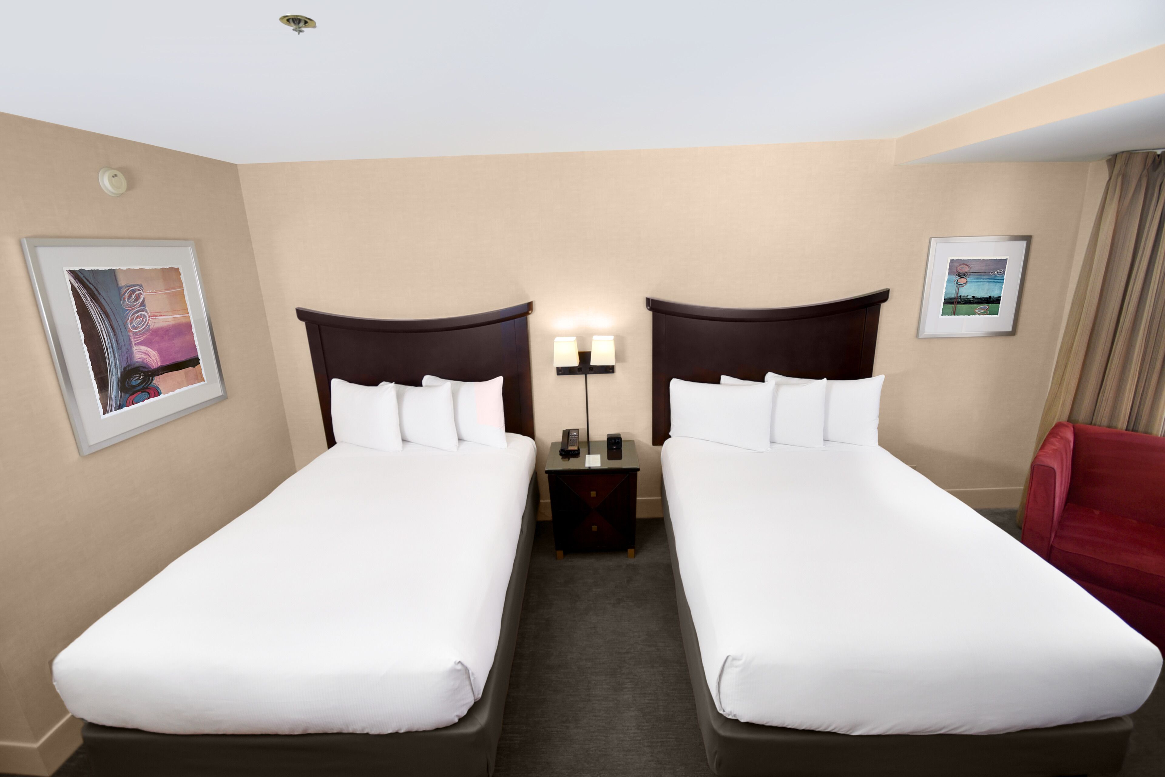Ein Hotelzimmer mit zwei Einzelbetten, einem Nachttisch mit Lampe und einem roten Sessel.