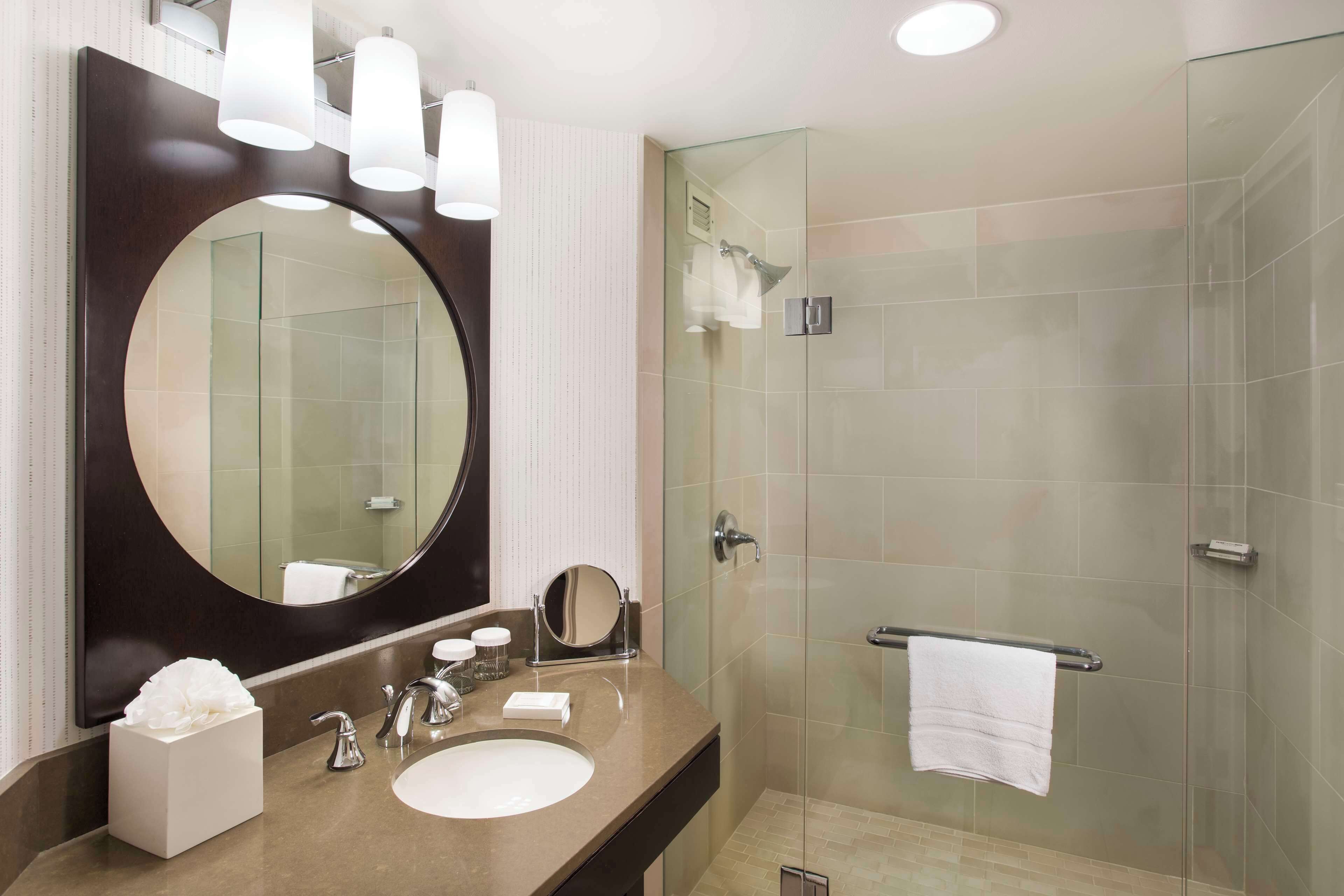 A modern bathroom with a large mirror, a round vanity, a glass shower enclosure, and a towel rack.