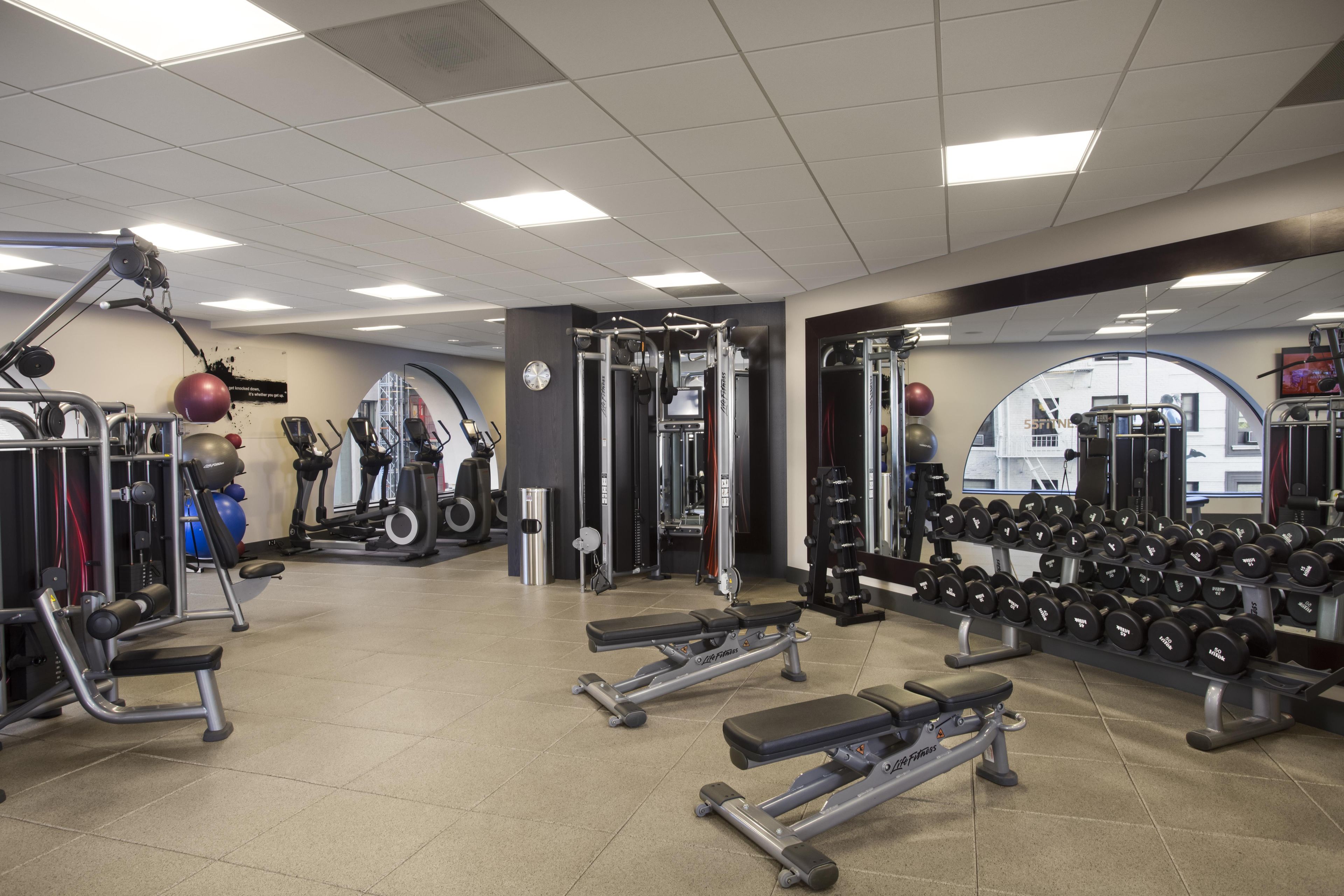 Un gimnasio con diversos equipos de ejercicio, incluyendo cintas de correr, máquinas de pesas y mancuernas.