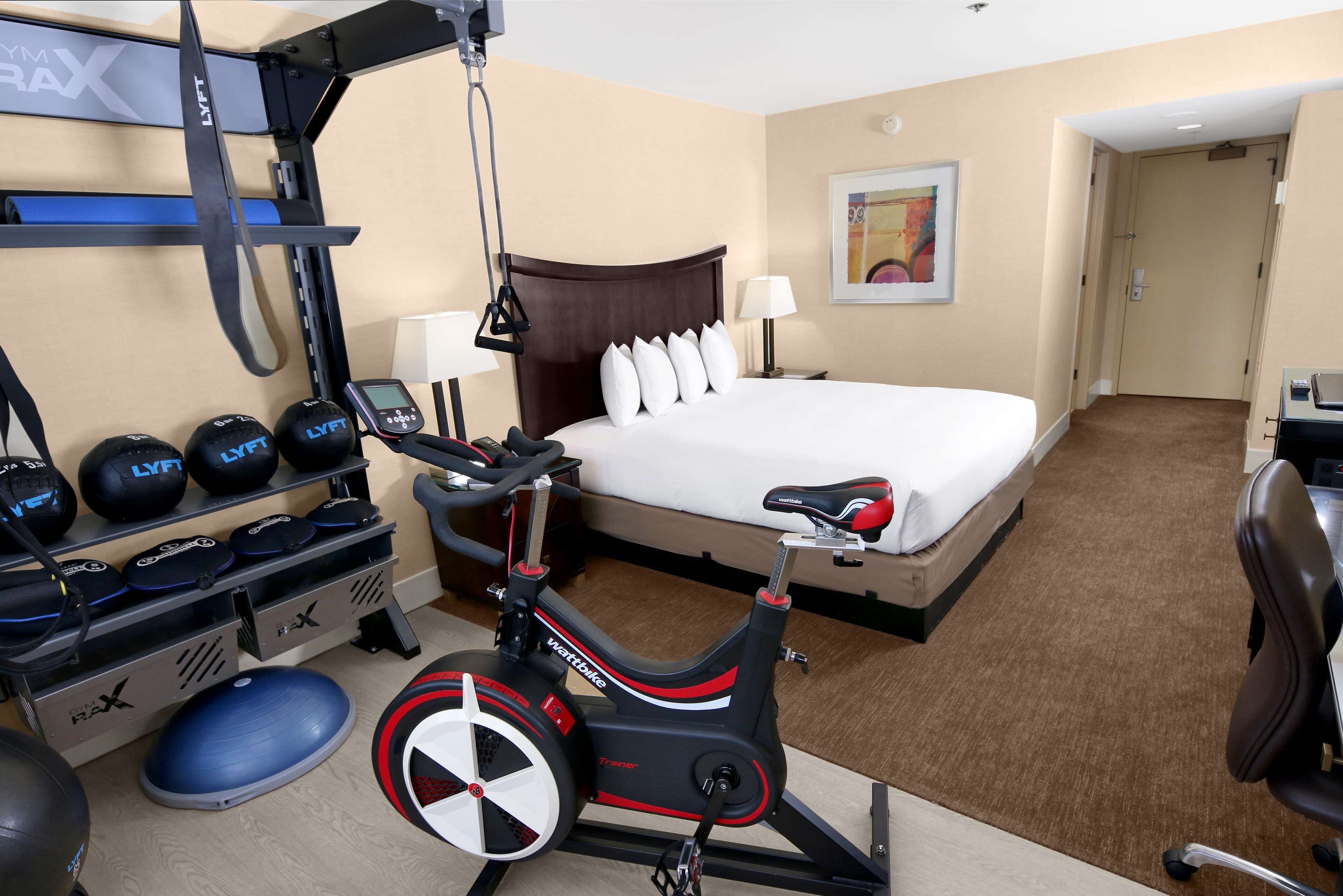 Una habitación de hotel con cama, equipo de ejercicio y un escritorio con silla.