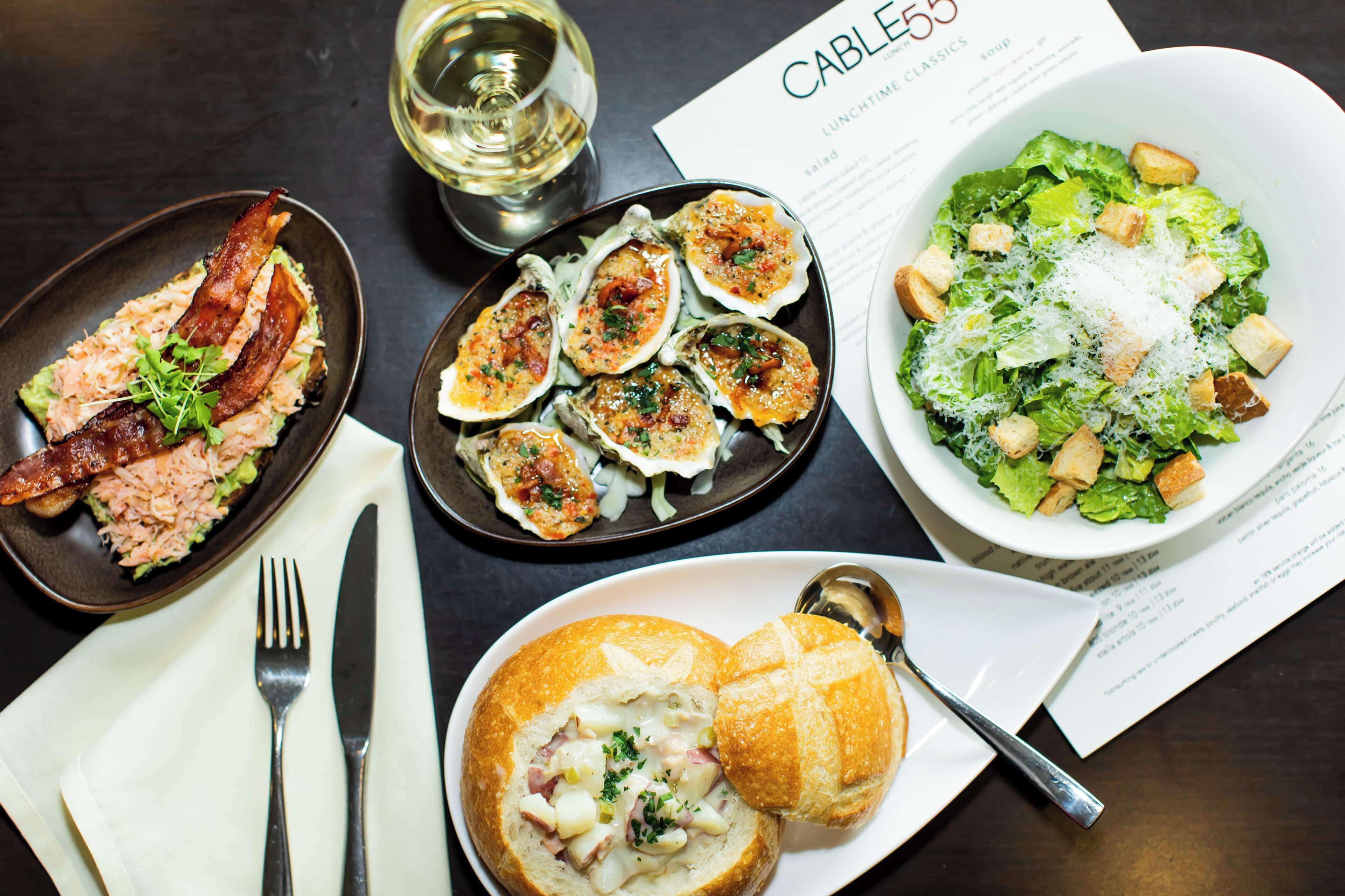 A table with various dishes including oysters, salad, and soup, along with cutlery and a menu.