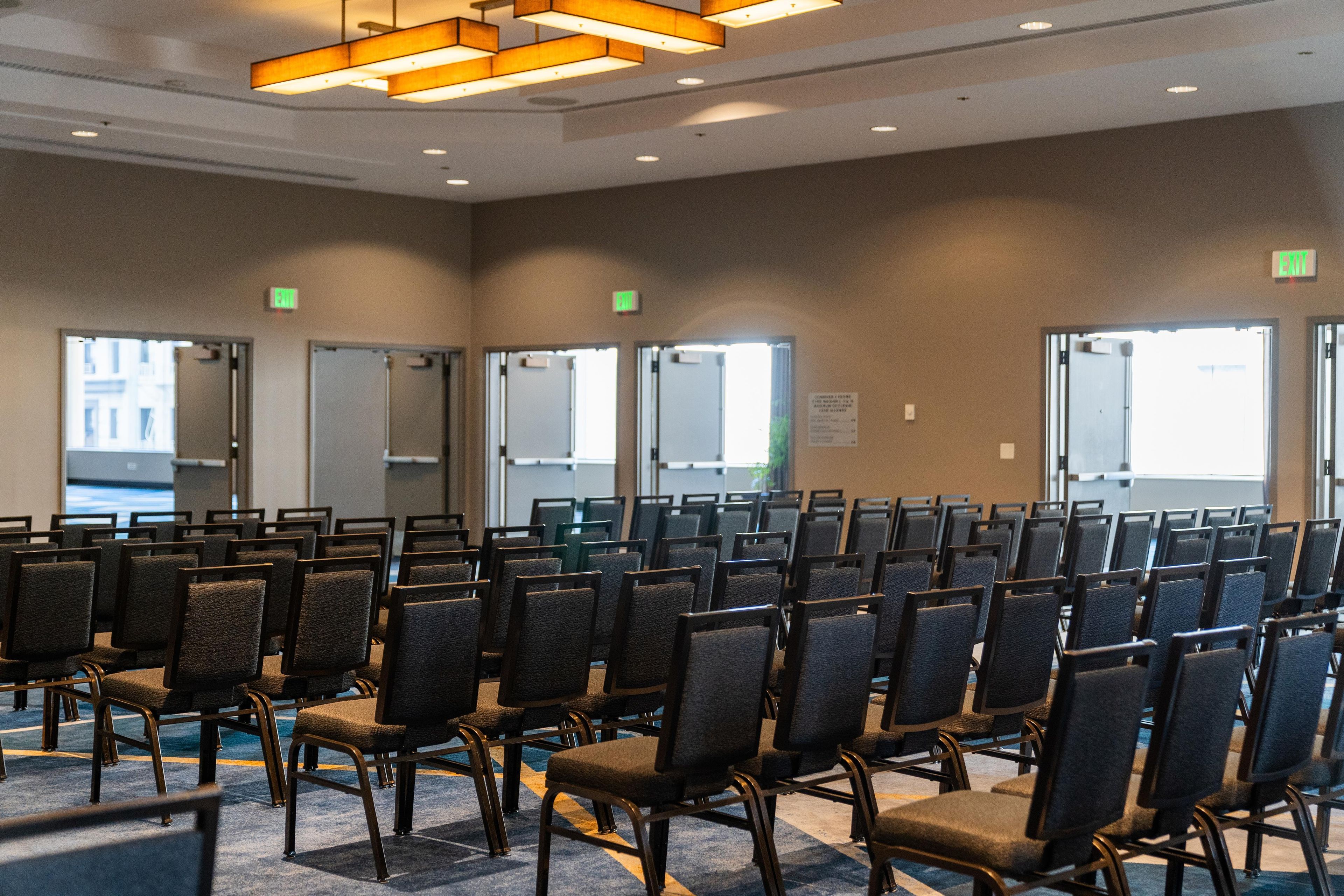 A conference room with rows of chairs, exit signs, and a view of the outside.