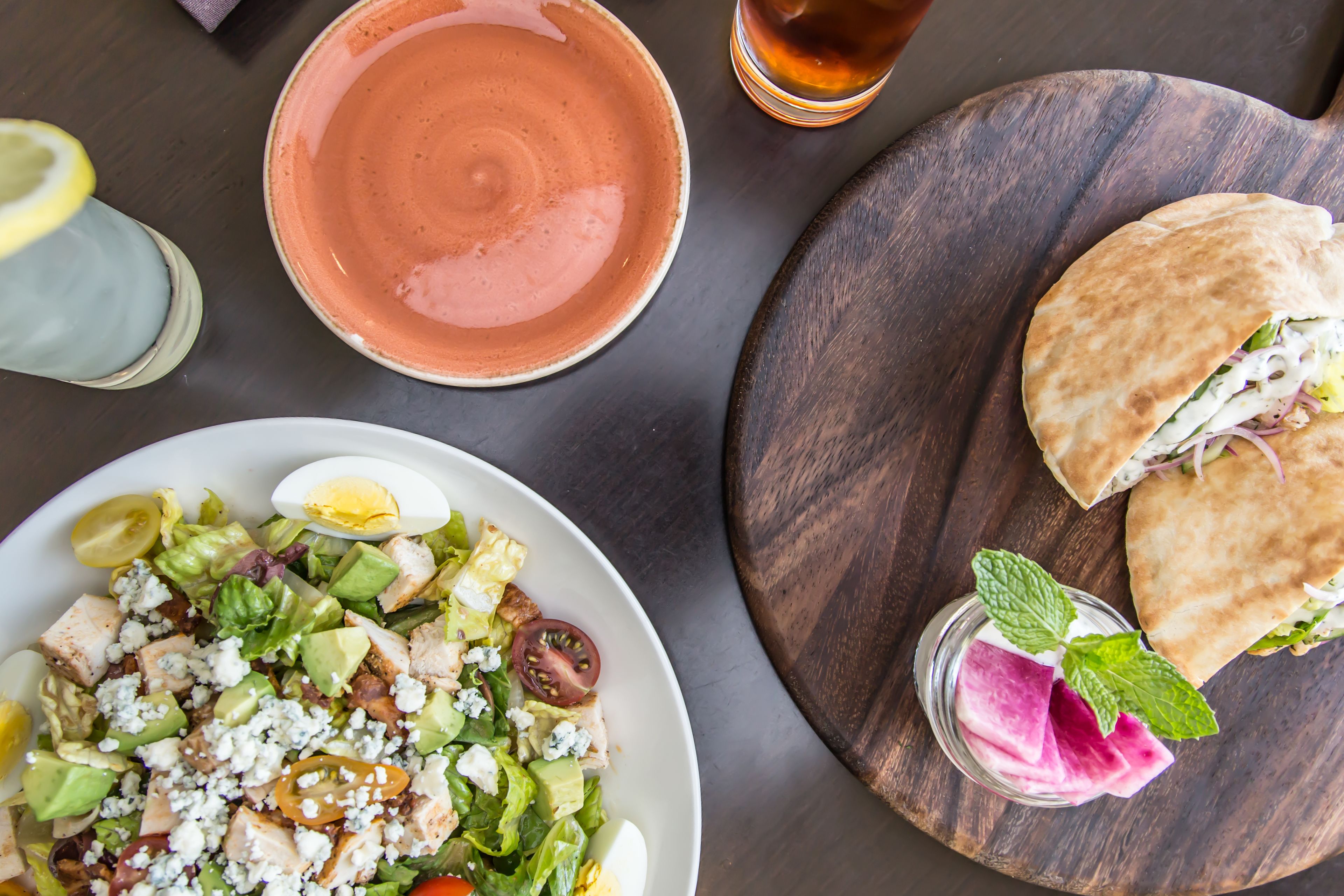 A table with a plate of salad, a bowl, a glass of drink, and a piece of flatbread.