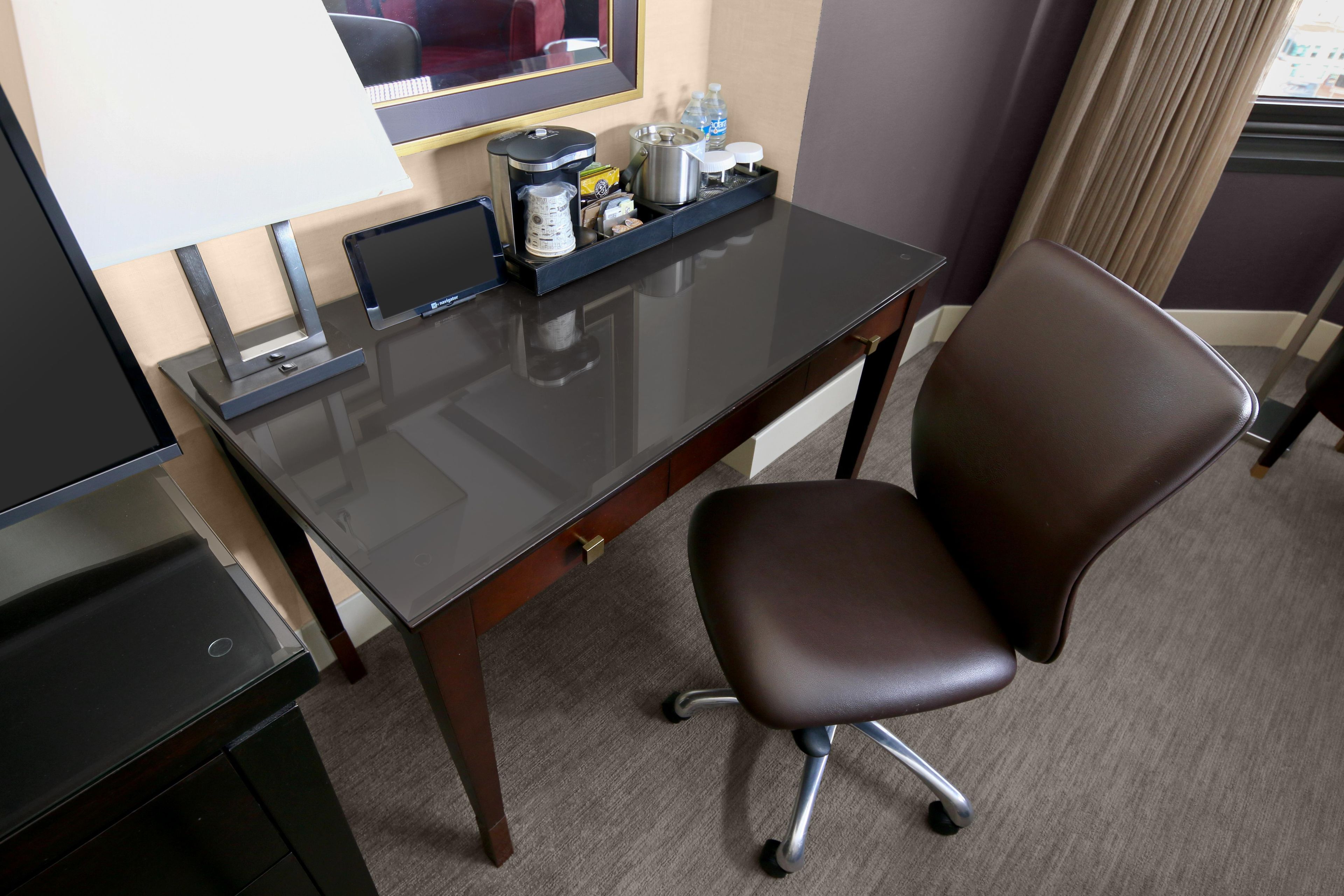 A hotel room with a desk, chair, television, and a coffee maker.