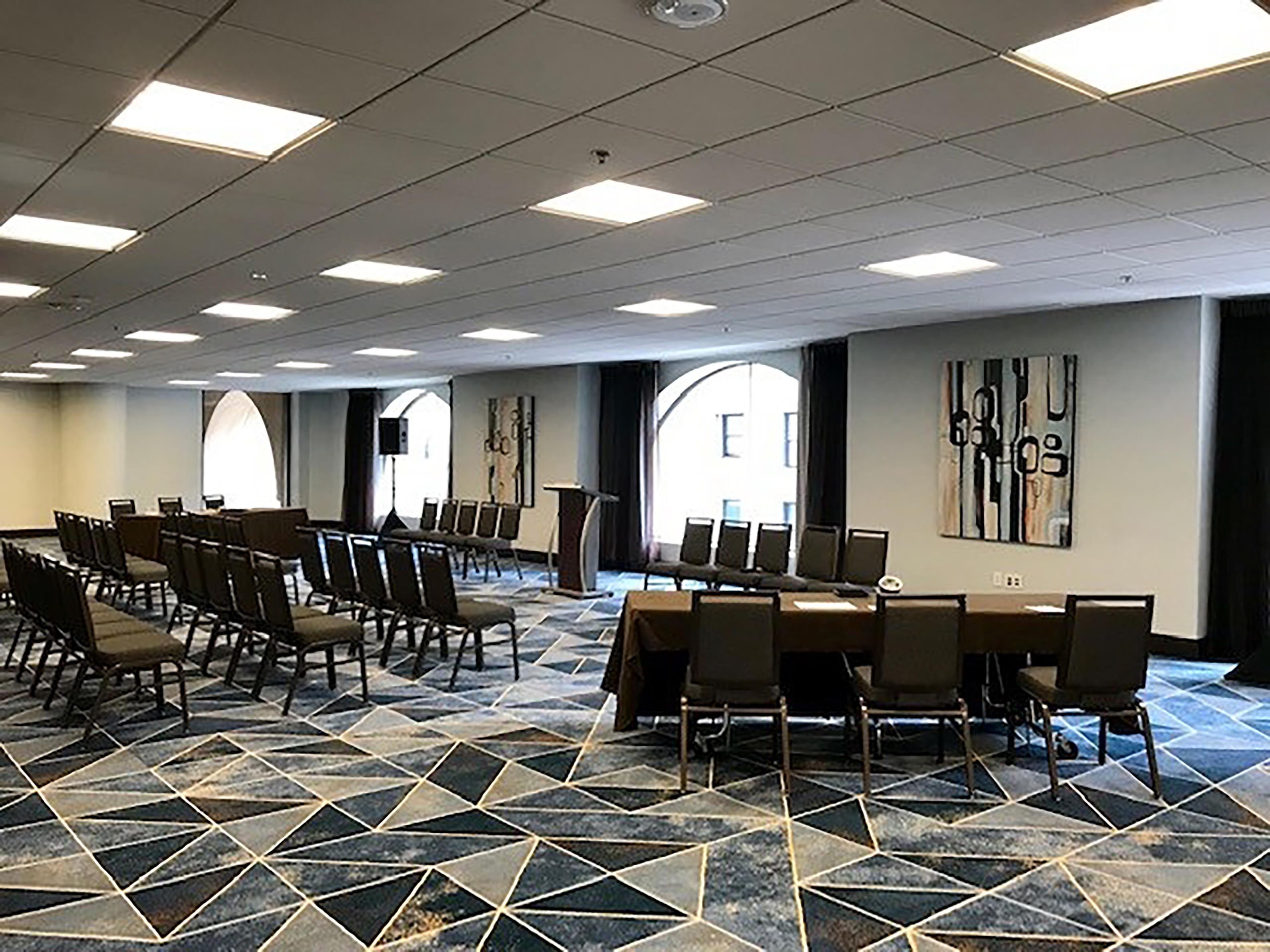 Un salón de conferencias con suelo de diseño geométrico, varias mesas, sillas y un amplio ventanal que proporciona luz natural.