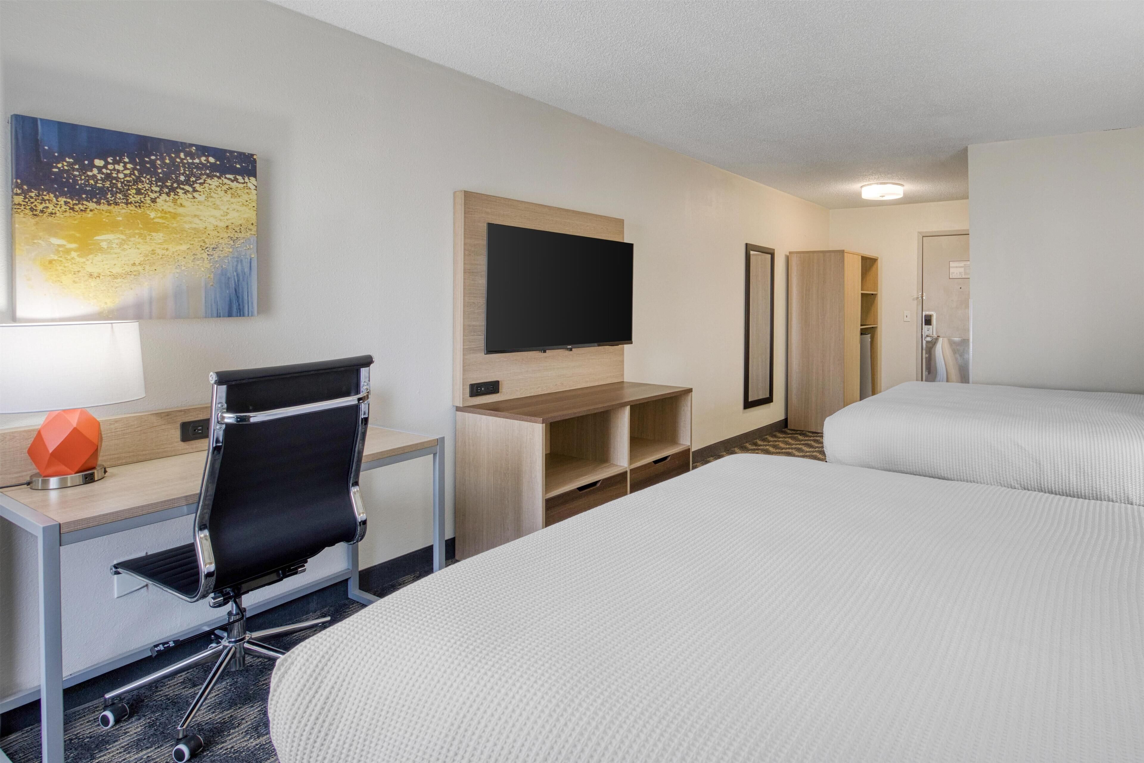 A hotel room with a bed, a desk with a chair, a flat-screen TV mounted on the wall, and a wardrobe.