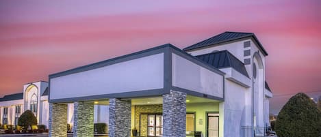 A modern hotel with a covered entrance, stone pillars, and a well-lit facade.