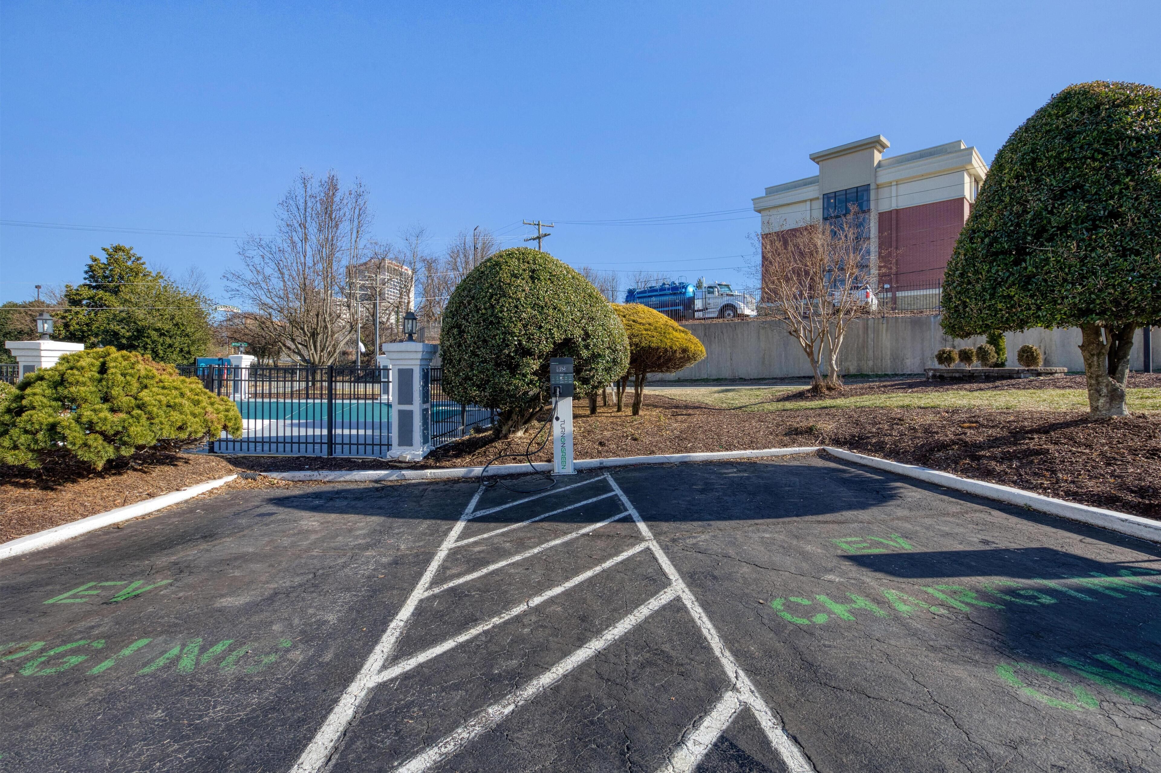 A parking lot with marked spaces, a blue fence, and a building in the background.
