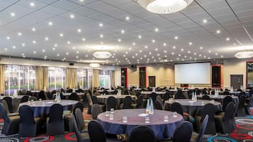 Un salón de conferencias con mesas redondas, sillas, una pantalla de proyector y un ventanal grande.
