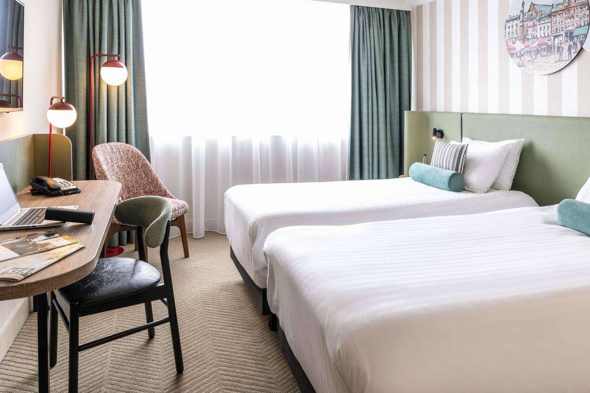 Habitación de hotel con dos camas, un escritorio con una computadora portátil, una silla y una lámpara.