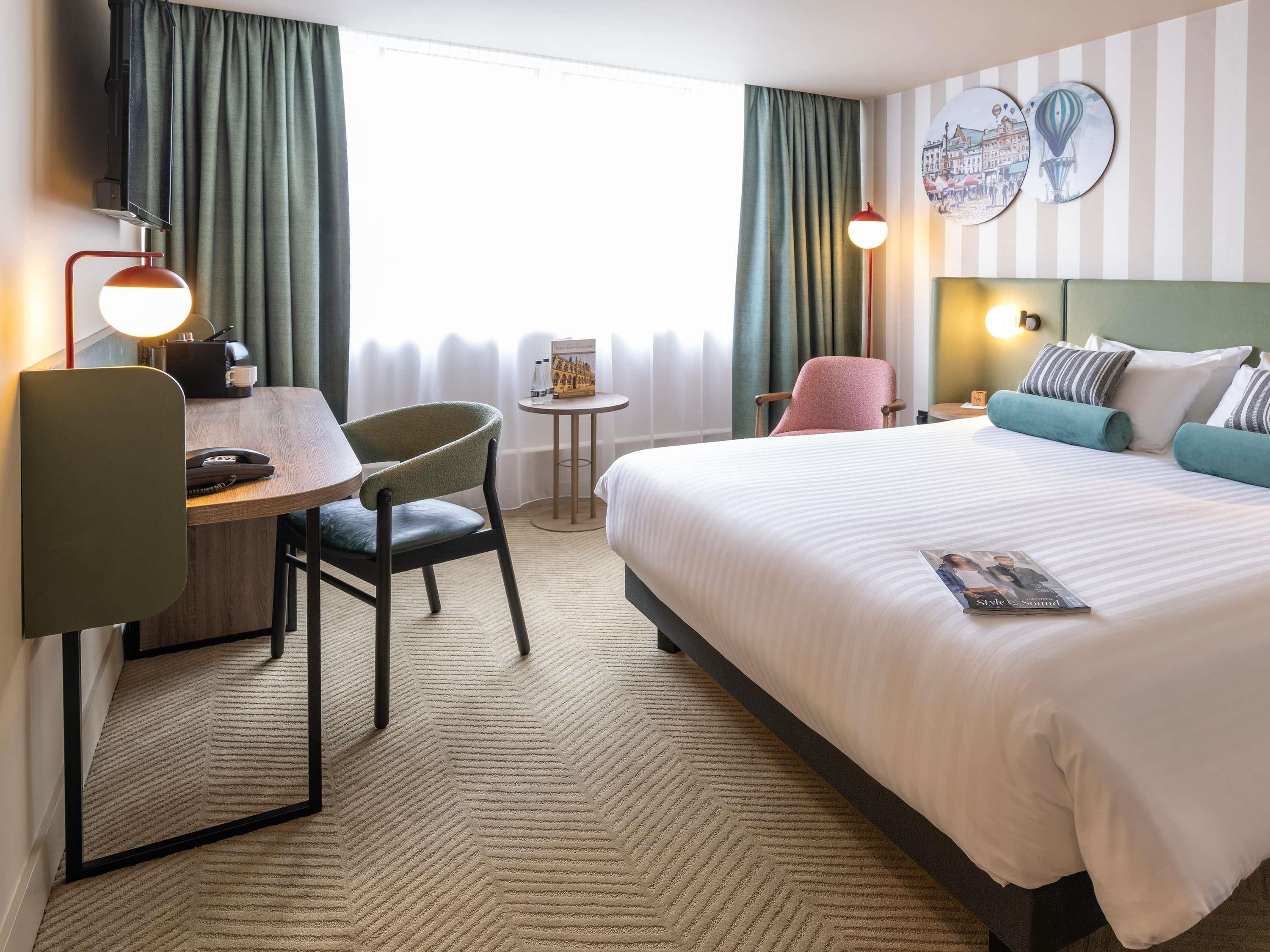 Una habitación de hotel con una cama, un escritorio con una silla, una mesita y una lámpara.