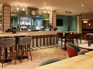 A bar area with stools, a counter, and a clock. - Mercure Northampton (Northampton)