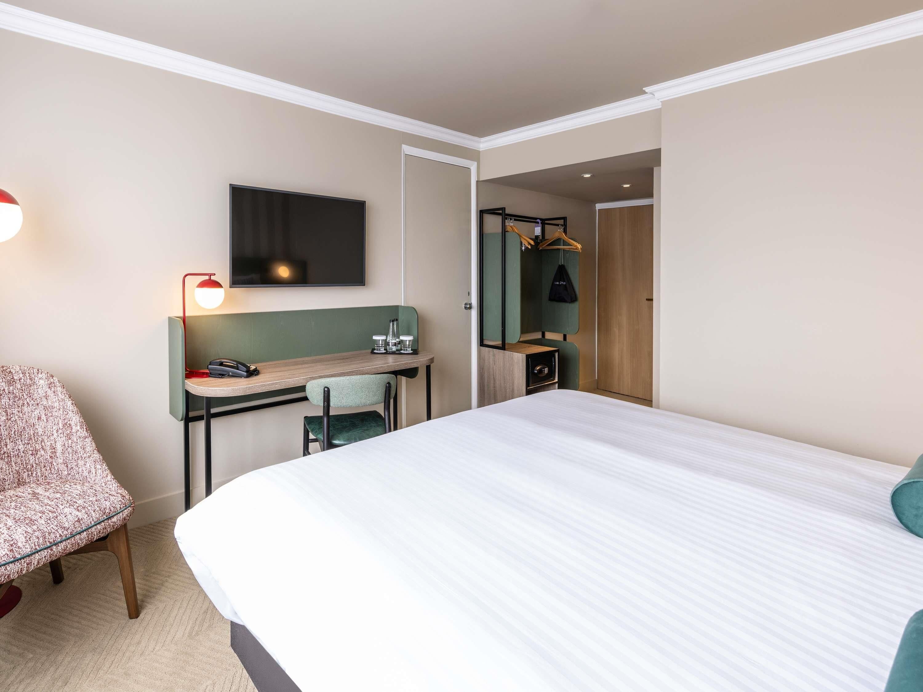 Una habitación de hotel con cama, escritorio con silla, televisión y espejo.