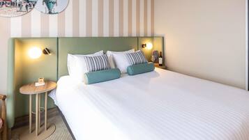 A hotel room with a bed, striped wall, round bedside table, and a wall-mounted light.