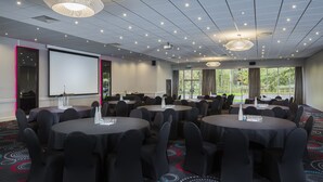 A conference room with multiple round tables, black chairs, and a large projector screen.