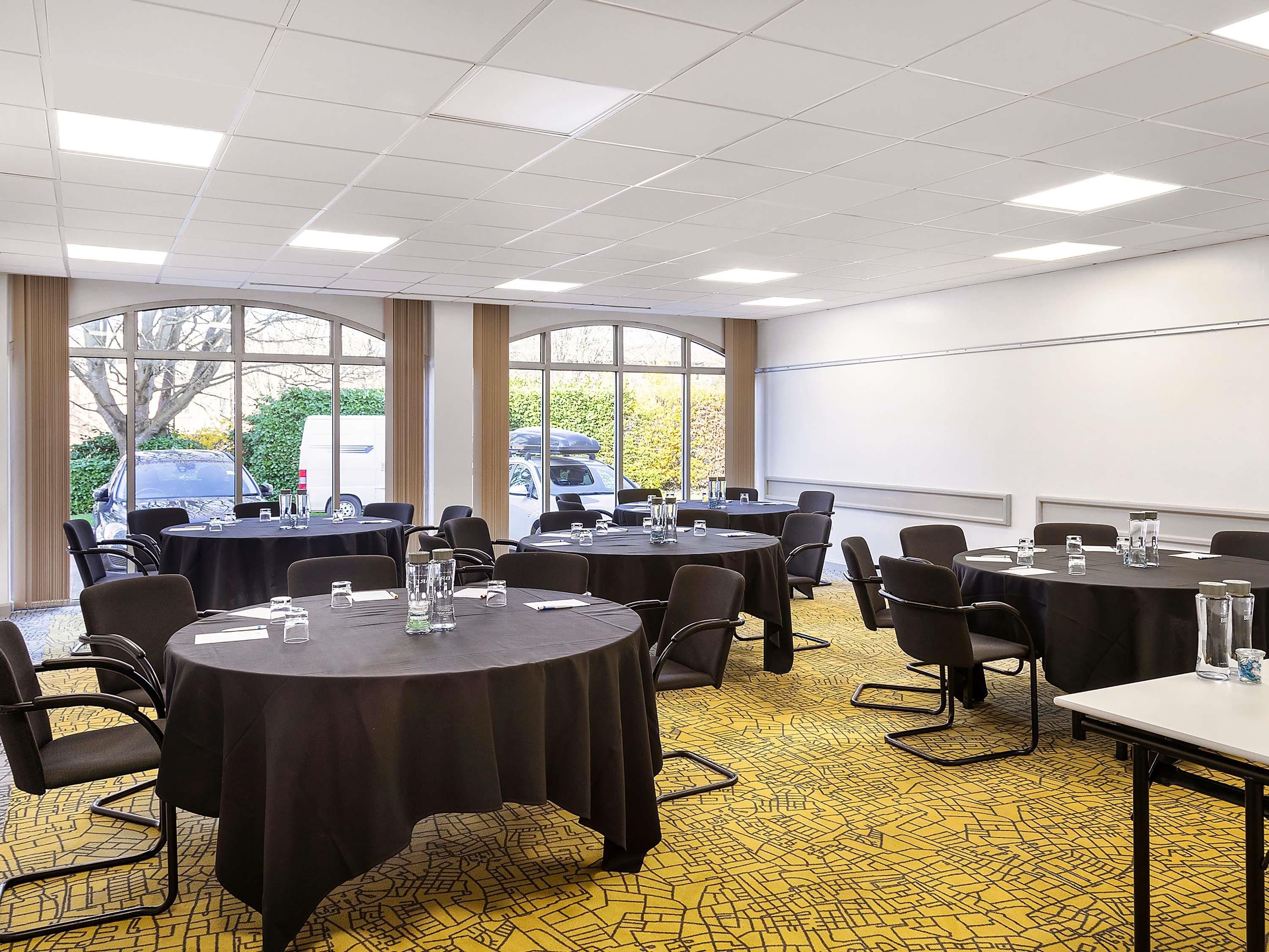 Un salón de conferencias con varias mesas, sillas y una pantalla de proyector.