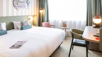 A hotel room with a large bed, a desk, a chair, a small table with a lamp, and a wall art piece.