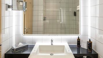 Une salle de bain moderne avec un grand miroir, des carreaux blancs, un plan de travail noir et un lavabo blanc.